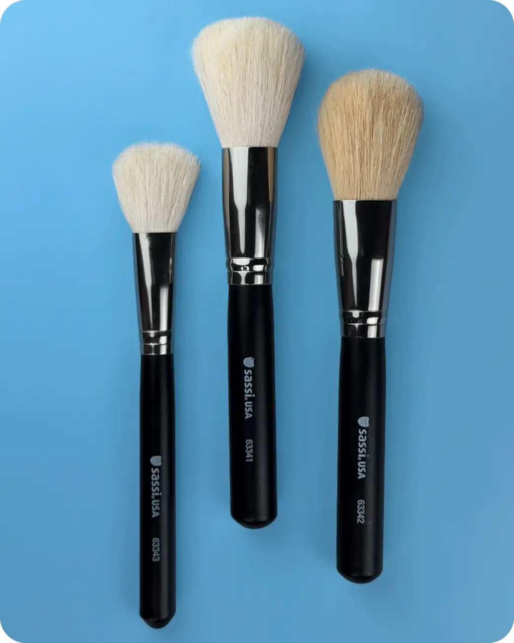 Three Sassi makeup brushes on a blue background