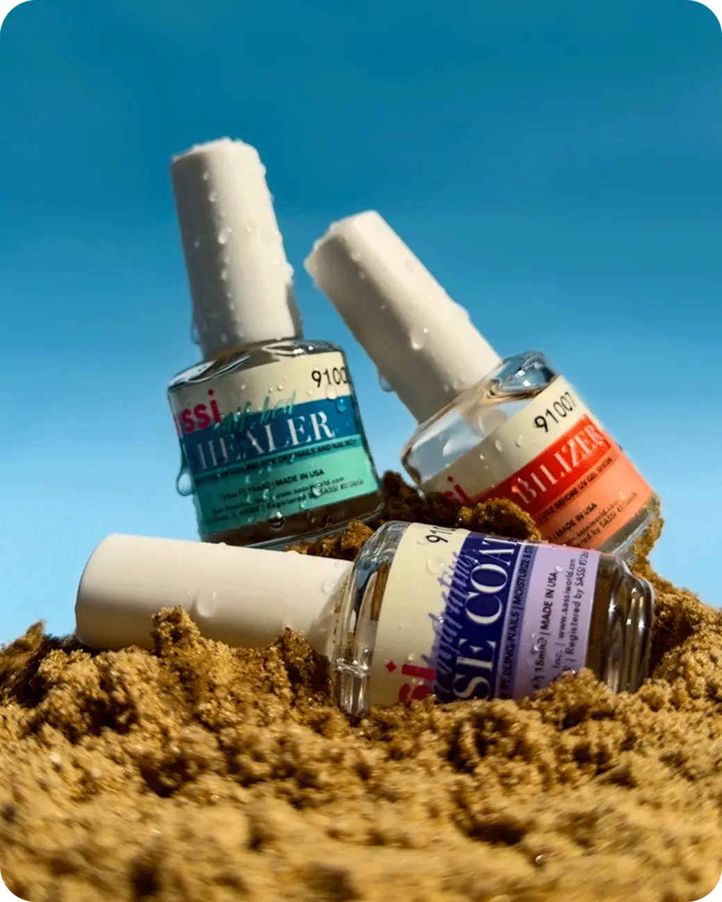 Sassi nail products styled in sand against a blue sky